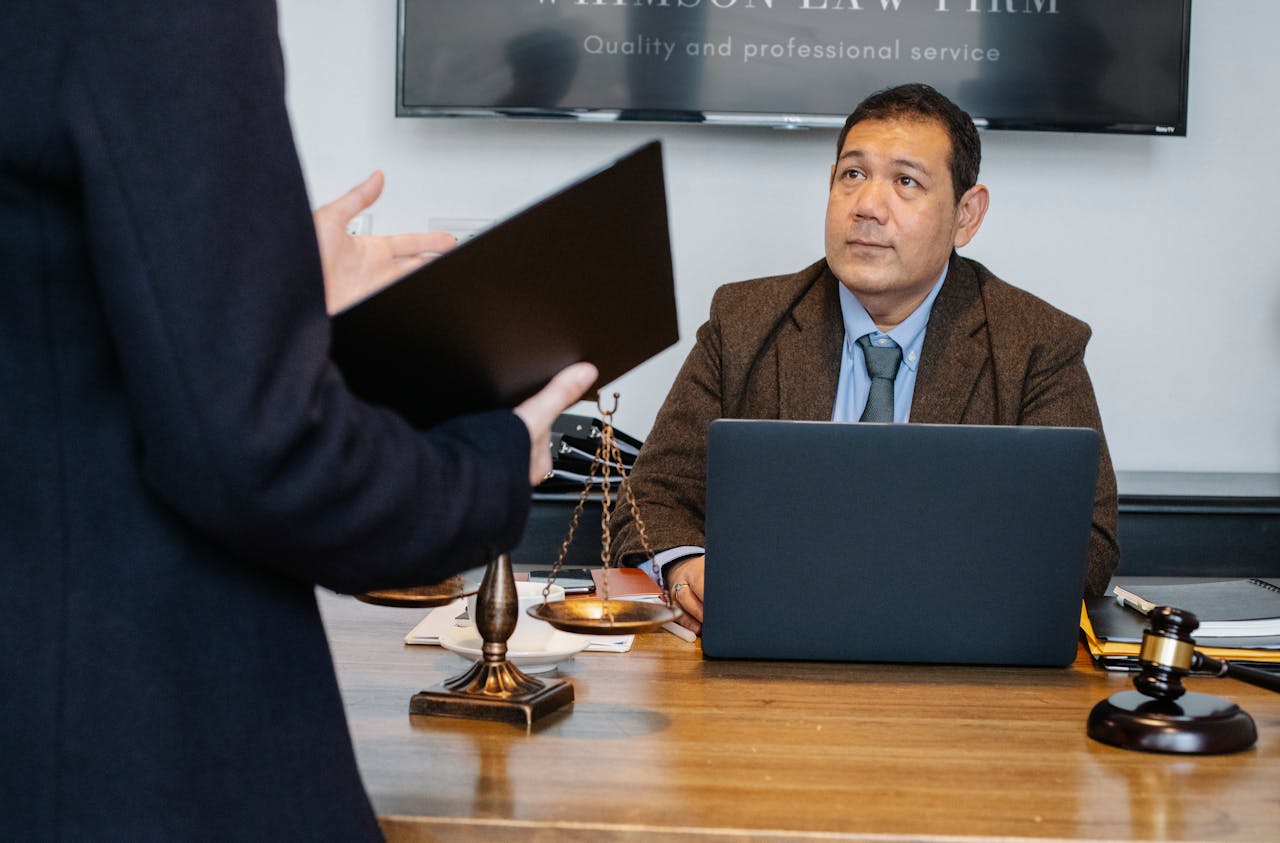 why-choose-us Crop unrecognizable employee representing new case details to concentrated middle aged ethnic lawyer sitting at table with laptop gavel and justice scales
