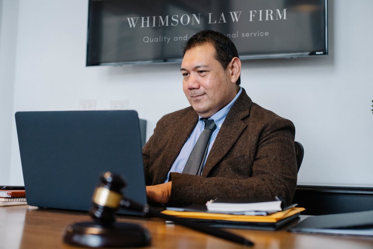 creative A lawyer working on a laptop in a legal office, wearing a suit and tie, with a gavel on the desk.
