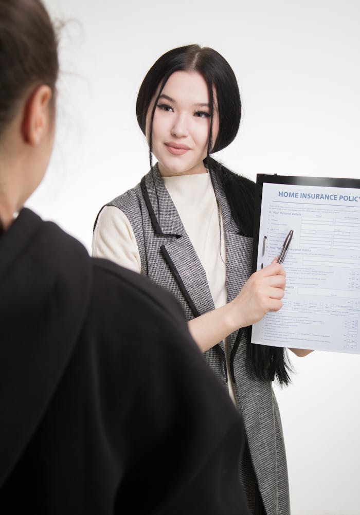 Young Asian businesswoman explaining home insurance policy to client, highlighting details with pen.