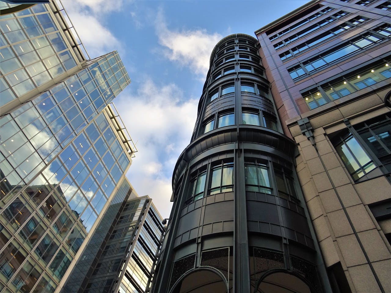 Low angle view of modern skyscrapers with glass facades against a blue sky with clouds.